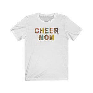 以下が含まれることがあります： レオパード柄のカラフルな文字で「CHEER MOM」と書かれた白いTシャツです。
