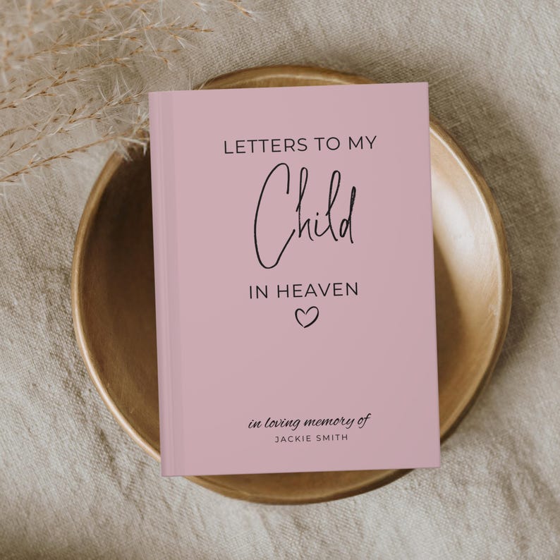 May include: A pink journal with the text "Letters to My Child in Heaven" and a small heart symbol. The text "in loving memory of Jackie Smith" is printed below the heart.