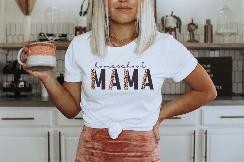 Op de afbeelding: Wit T-shirt met de tekst "homeschool MAMA" in zwarte letters met een luipaardprint.