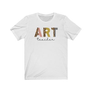 K&ouml;nnte beinhalten: Wei&szlig;es T-Shirt mit dem Wort "ART" in bunten Buchstaben mit Leopardenmuster. Das Wort "teacher" ist darunter in Kursivschrift geschrieben.