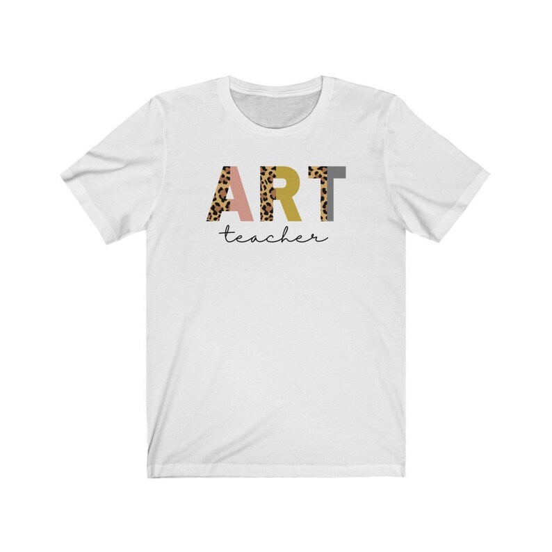 K&ouml;nnte beinhalten: Wei&szlig;es T-Shirt mit dem Wort "ART" in bunten Buchstaben mit Leopardenmuster. Das Wort "teacher" ist darunter in Kursivschrift geschrieben.
