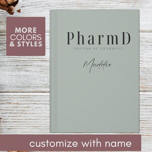 May include: A light green journal with the text "PharmD Doctor of Pharmacy" and the name "Maddie" written in cursive. The journal is on a white wooden background.