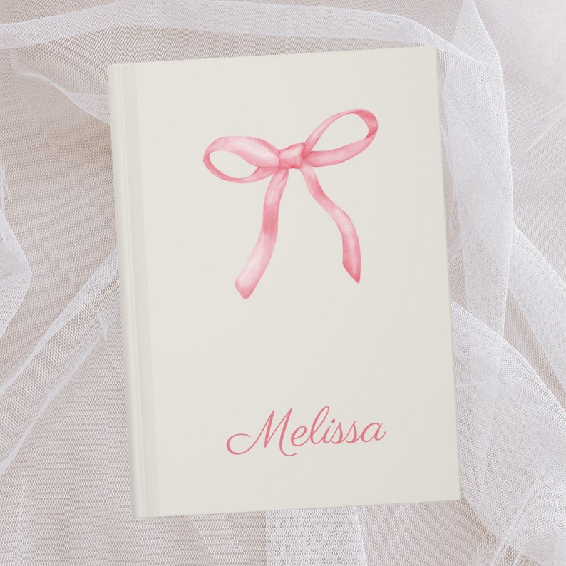 May include: A white journal with a pink watercolor bow and the name "Melissa" written in pink cursive.