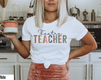 May include: White t-shirt with the text "Theatre TEACHER" in colorful letters with a leopard print pattern.