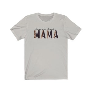 Op de afbeelding: Een lichtgrijs T-shirt met de tekst "homeschool MAMA" gedrukt op de voorkant. Het woord "MAMA" staat in zwarte letters met een luipaardprint.