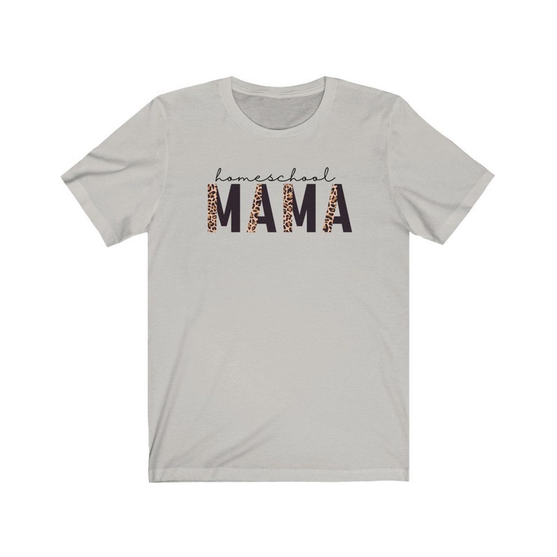 Op de afbeelding: Een lichtgrijs T-shirt met de tekst "homeschool MAMA" gedrukt op de voorkant. Het woord "MAMA" staat in zwarte letters met een luipaardprint.