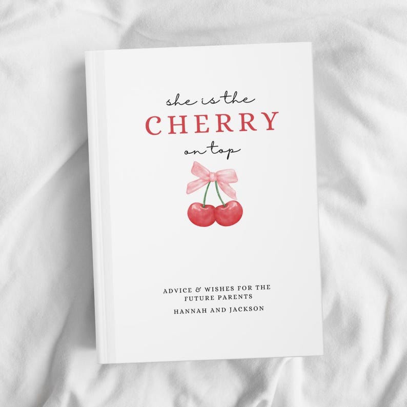 May include: A white book with the text "she is the CHERRY on top" in black and red lettering. A pink bow with two red cherries is illustrated above the text. The text "ADVICE & WISHES FOR THE FUTURE PARENTS HANNAH AND JACKSON" is printed in black at the bottom of the book.