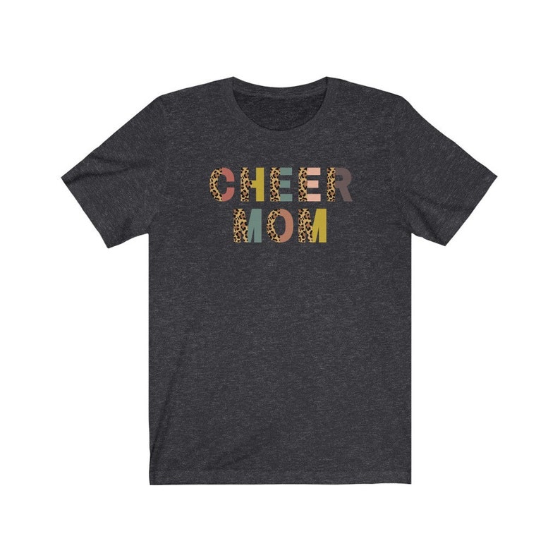 以下が含まれることがあります： レオパード柄のカラフルな文字で「CHEER MOM」と書かれたダークヘザーグレーのTシャツです。