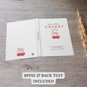 May include: A white book with a pink and red cherry illustration on the front cover. The title of the book is "She is the Cherry on Top". The back cover has the text "Advice & Wishes for the Future Parents Hannah and Jackson".