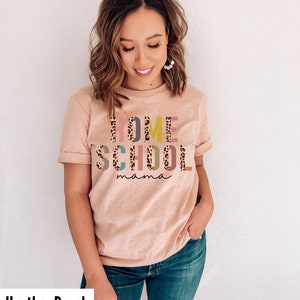 May include: A heather peach colored t-shirt with the text "HOME SCHOOL mama" in colorful letters with a leopard print pattern.