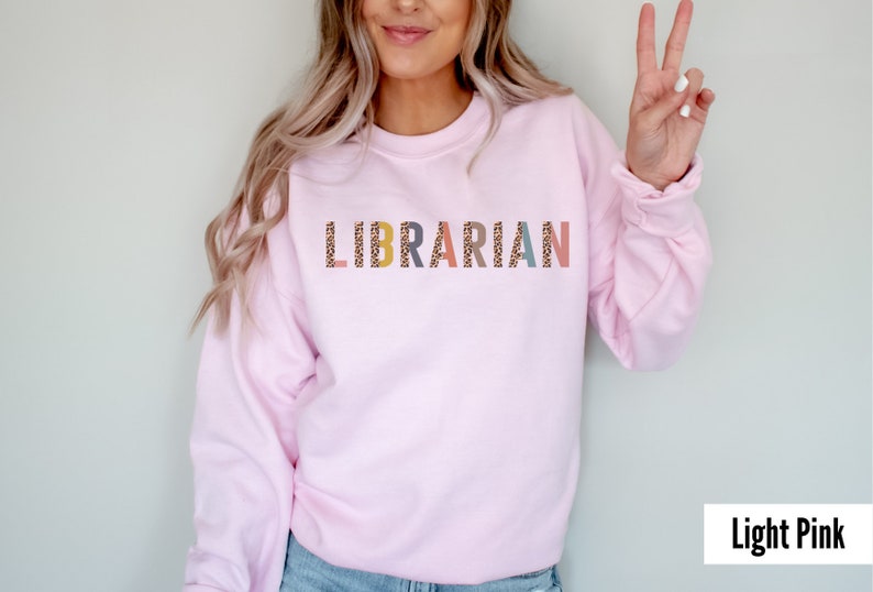 Peut inclure: Un sweat-shirt rose p&acirc;le avec le mot "LIBRARIAN" imprim&eacute; sur le devant en lettres color&eacute;es avec un motif l&eacute;opard.