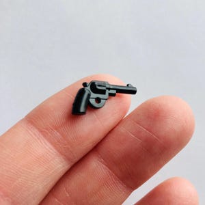 May include: A small, black plastic toy gun. The gun is a revolver with a barrel and a handle.