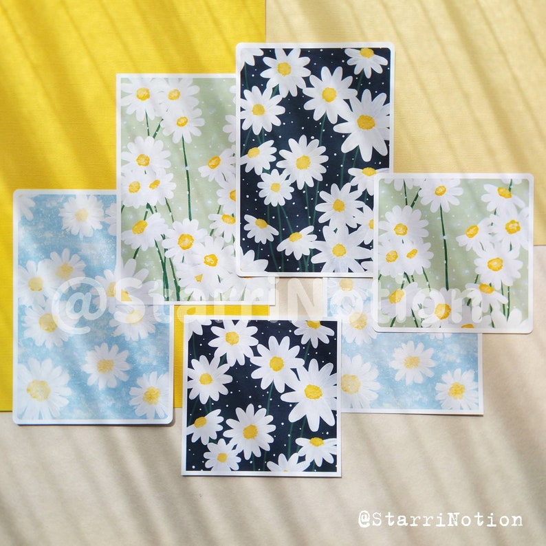 May include: Set of six illustrated cards featuring white daisies on different coloured backgrounds. The backgrounds include green, blue, black, and white. The cards are perfect for adding a touch of whimsy to any space.