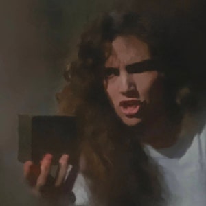 May include: A person with long, curly hair, wearing a white shirt, holds a dark rectangular object. The person's expression is one of surprise or concern, with their mouth open. The background is a dark, blurred environment.