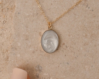 May include: A gold chain necklace with a white oval pendant. The pendant has a marbled pattern.