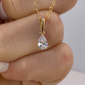 May include: A gold chain necklace with a teardrop-shaped pendant featuring a clear cubic zirconia stone.