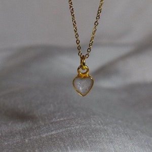 May include: A gold chain necklace with a small heart-shaped pendant. The pendant is clear and has a sparkly, glittery finish.