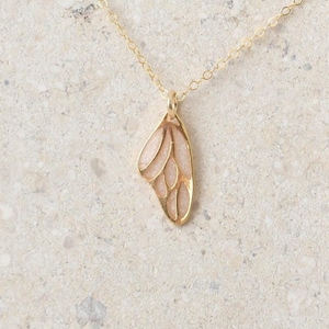 May include: A gold chain necklace with a delicate butterfly wing pendant. The pendant is made of gold and has a light pink enamel finish.