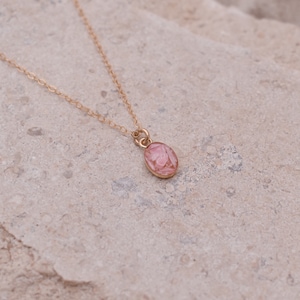 Op de afbeelding: Een delicate gouden ketting met een kleine roze ovale hanger.