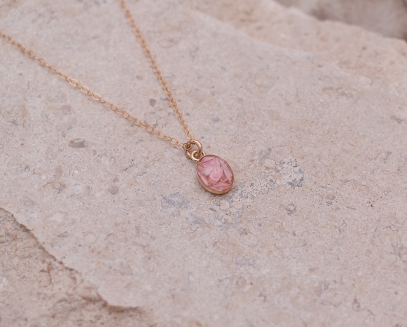 Op de afbeelding: Een delicate gouden ketting met een kleine roze ovale hanger.