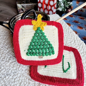 May include: Two square, crocheted Christmas potholders. Each potholder has a white center with a red border. One features a green Christmas tree with a yellow star, the other has a green hook design. The potholders are on a white, textured surface.