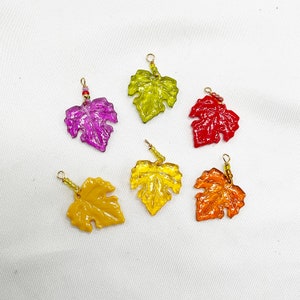 May include: Six glass leaf charms in various colors, including purple, green, red, and yellow. Each charm has a gold loop for hanging.
