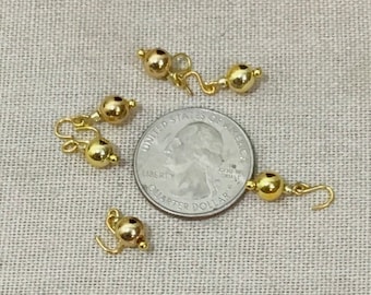 May include: Four gold-toned metal clasps with a loop and a ball on each end. The clasps are shown next to a US quarter for size comparison.