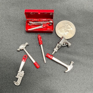 Pode incluir: Uma caixa de ferramentas vermelha contendo uma seleção de ferramentas em miniatura, incluindo um martelo, uma chave, uma chave de fenda, uma serra e uma furadeira. As ferramentas são todas prateadas com alças vermelhas.