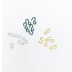 May include: Assortment of S-shaped hooks in green, silver, and gold. The hooks are small and are arranged in groups on a white surface.
