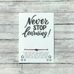 May include: A white card with black text that reads "Never Stop Learning!" and a red string bracelet with black beads. The card also includes instructions for making a wish with the bracelet.
