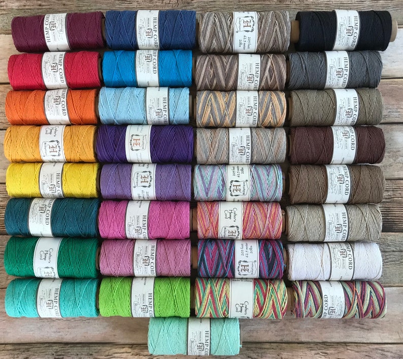 Puede incluir: Una colecci&oacute;n de 24 carretes de cuerda de c&aacute;&ntilde;amo en varios colores y patrones, incluyendo natural, rojo, azul, verde, amarillo y marr&oacute;n. Cada carrete est&aacute; etiquetado con "Hemp Cord" y tiene un patr&oacute;n diferente.