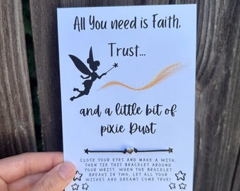 Puede incluir: Una tarjeta blanca con la silueta negra de un hada con varita, un rastro de purpurina dorada y el texto All You need is Faith, Trust... and a little bit of pixie Dust. Se incluye una pulsera de cordón negro con un pequeño dije de corazón plateado.