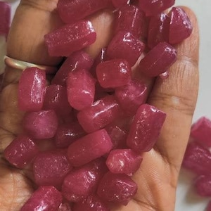 Pode incluir: Uma mão segurando um monte de pequenas pedras preciosas facetadas cor-de-rosa. As pedras preciosas são todas de tamanho e forma semelhantes, e têm um acabamento liso e polido.