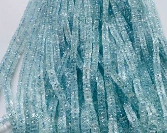 May include: A strand of light blue aquamarine beads, each bead is faceted and has a square shape. The beads are strung on a thin thread and are arranged in a loose pile.