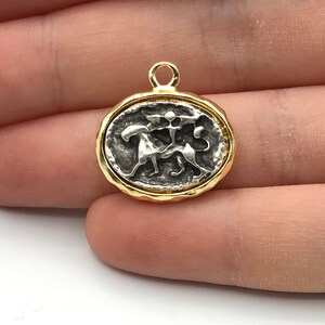 May include: Three gold-toned metal charms featuring a silver-toned design of two lions facing each other. The charms are round and have a textured edge.