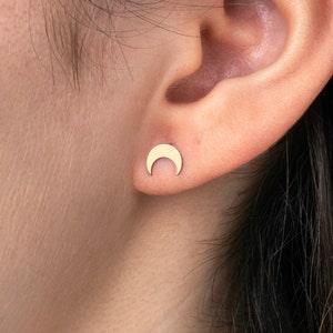 May include: A pair of gold crescent moon stud earrings. The earrings are small and delicate, and they are perfect for everyday wear.