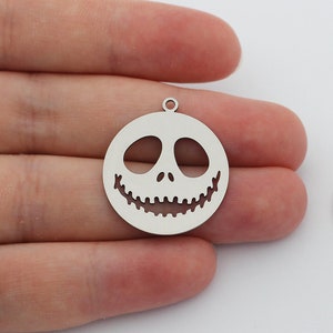 May include: Two silver metal charms featuring a cutout design of a smiling jack-o'-lantern face.
