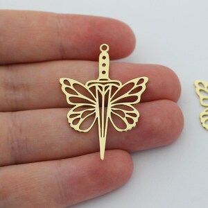 May include: Two gold-colored metal charms in the shape of a butterfly with a dagger in the center.