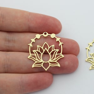 Puede incluir: Dos abalorios de metal de color dorado en forma de flor de loto con un círculo de pequeños puntos alrededor del exterior. Los abalorios están recortados y tienen un diseño delicado.