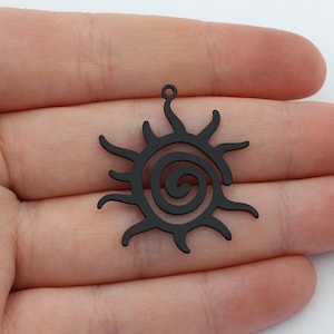 May include: Black metal pendant charm with a sun design featuring a spiral in the centre.