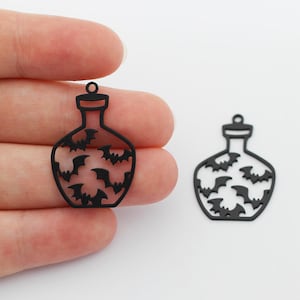 May include: Two black metal charms shaped like bottles with a bat design. The charms are approximately 5 cm tall and have a loop at the top for attaching to a necklace or bracelet.