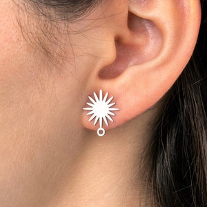 May include: Silver starburst earrings with a small circle dangling from the bottom.