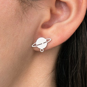 May include: A pair of silver earrings shaped like a planet with a ring around it.