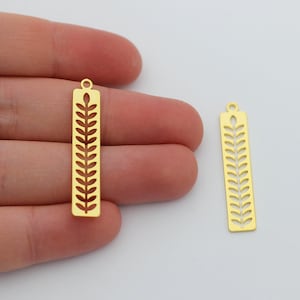 May include: Two gold-colored metal charms with a leaf design. The charms are rectangular and have a hole at the top for attaching to a necklace or bracelet.