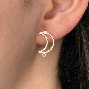 May include: Gold crescent moon earrings with a small dangling circle. The earrings are shown on a person's ear.