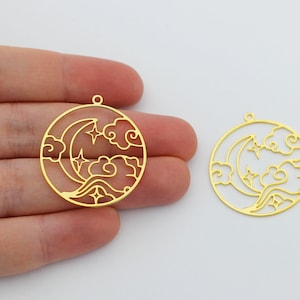 May include: Two gold-colored metal charms in the shape of a circle with a crescent moon, stars, and clouds design. The charms have a hole at the top for attaching to jewelry.