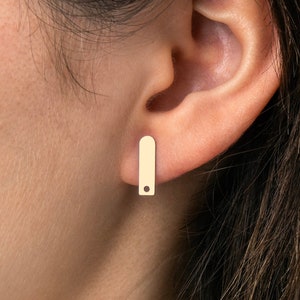 May include: A pair of gold bar earrings with a small round hole in the center of each bar.