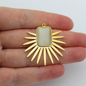 以下が含まれることがあります： 太陽の光線デザインにセットされた白い長方形の石を持つ金色のペンダント