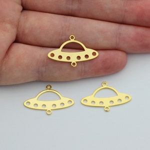 May include: Three gold-colored metal UFO charms with a hole at the top for hanging. Each charm has a rounded top and a flat bottom with a series of small holes around the edge.