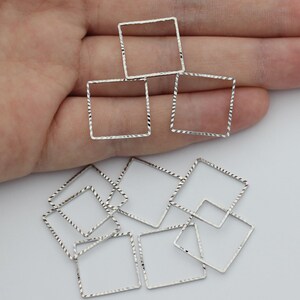 Op de afbeelding: Een verzameling zilverkleurige vierkante frames met een getextureerd, diamantgeslepen oppervlak. Deze open geometrische vormen zijn dun en lichtgewicht, met een herhalend patroon langs de randen dat het licht opvangt. Meerdere stuks getoond.